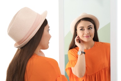 Young woman looking at her reflection in mirror on white background