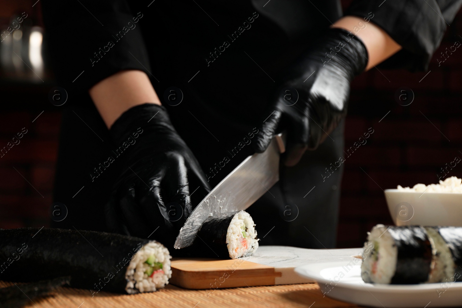 Photo of Chef in gloves cutting sushi roll at table, closeup