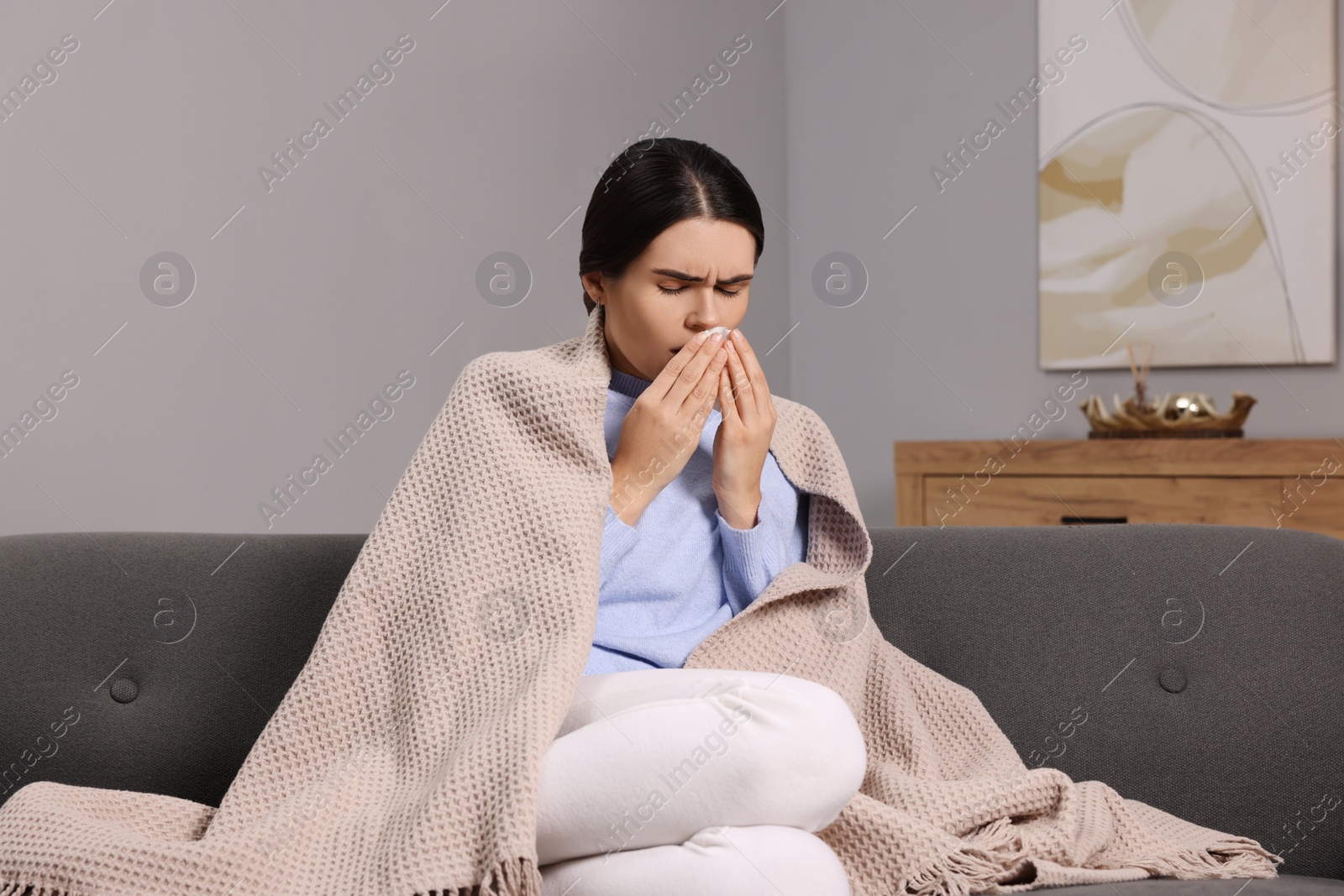 Photo of Woman coughing with tissue on sofa at home. Cold symptoms