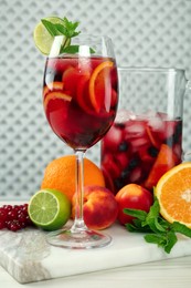 Photo of Glass and jug of Red Sangria with fruits on white wooden table