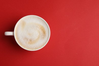 Tasty cappuccino in coffee cup on red background, top view. Space for text