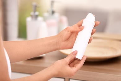 Photo of Young woman holding deodorant in bathroom, closeup