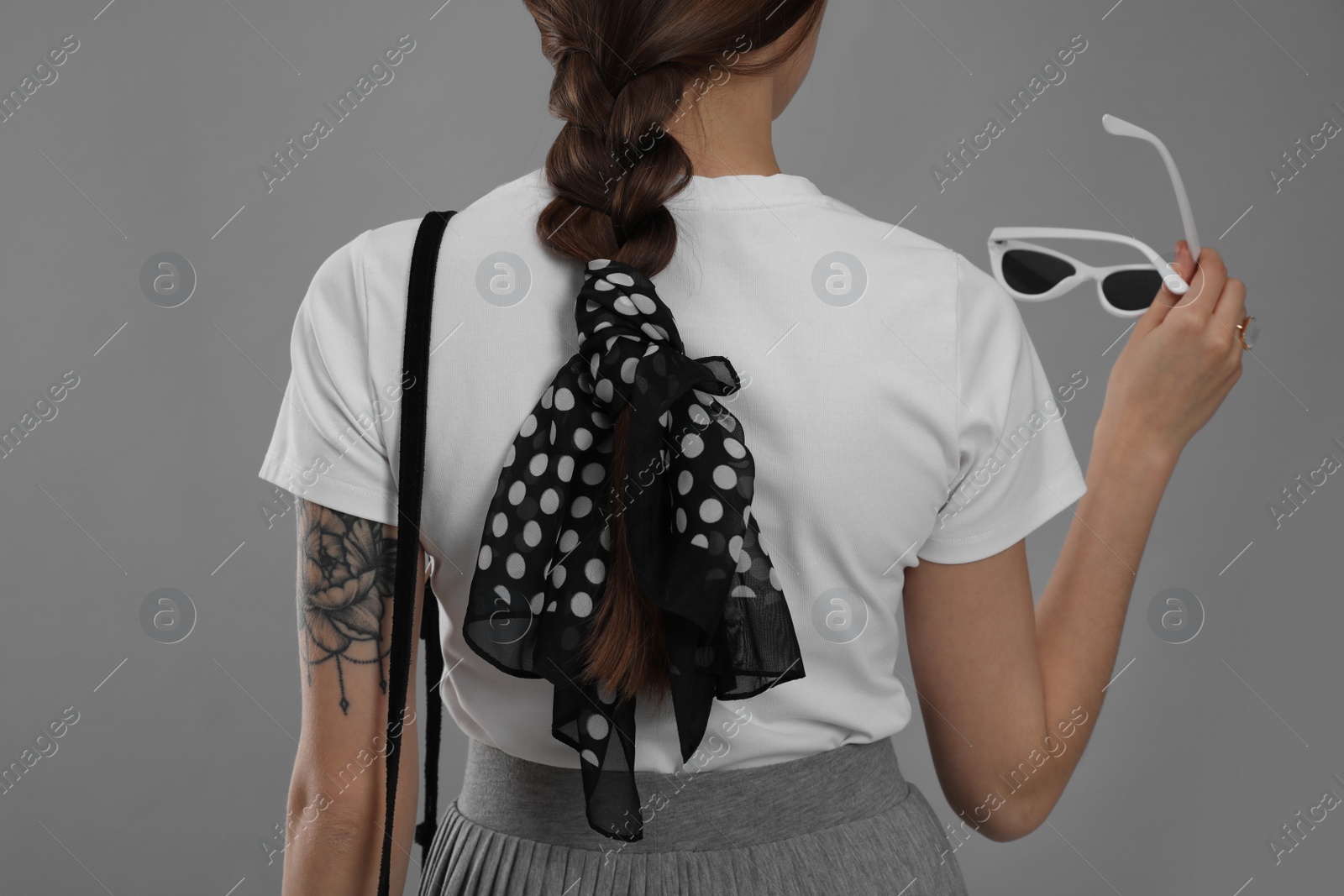 Photo of Young woman with sunglasses and stylish bandana on grey background, back view