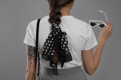 Young woman with sunglasses and stylish bandana on grey background, back view