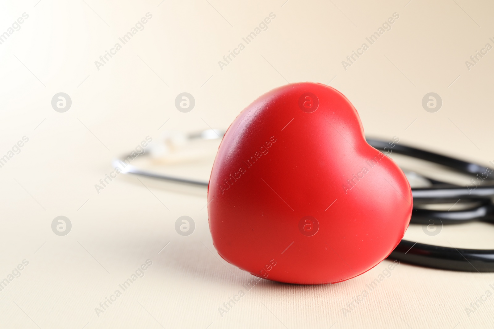 Photo of Stethoscope and red heart on beige background, closeup. Space for text