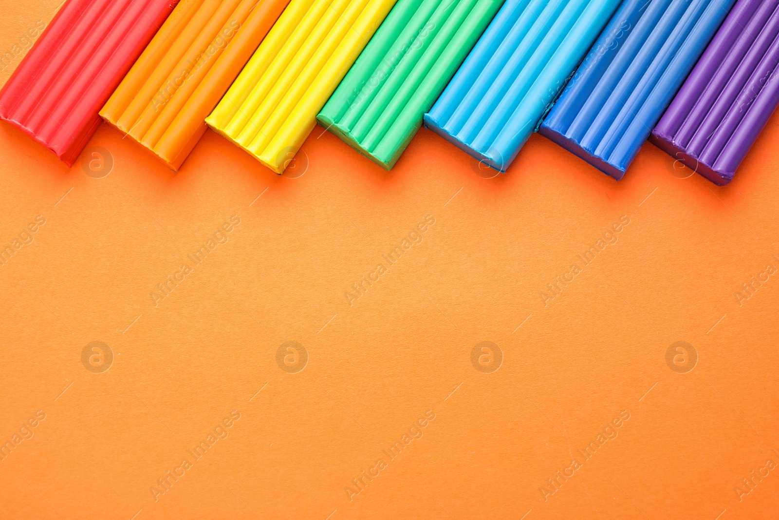 Photo of Colorful bars of modeling clay on orange background, flat lay with space for text. Rainbow palette