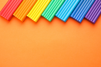 Photo of Colorful bars of modeling clay on orange background, flat lay with space for text. Rainbow palette