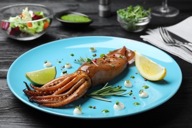 Photo of Delicious grilled squid served on black wooden table, closeup