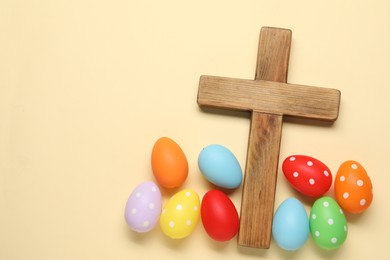 Wooden cross and painted Easter eggs on beige background, flat lay. Space for text