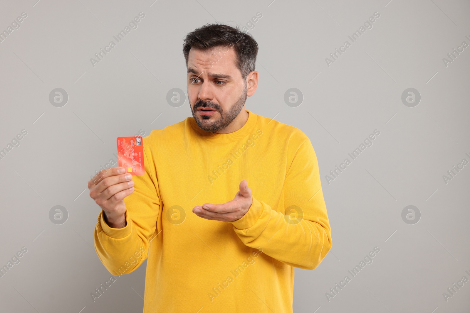 Photo of Confused man with credit card on grey background. Debt problem