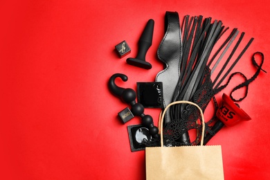 Shopping bag and different sex toys on red background, flat lay. Space for text