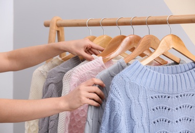 Woman choosing sweater on rack near color wall, closeup