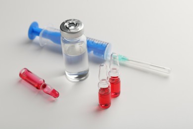 Photo of Glass ampoules with liquid and syringe on white background, closeup