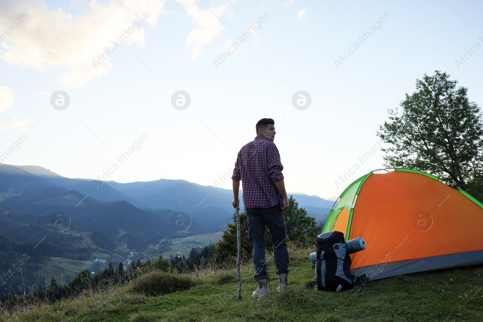 Photo of Tourist with backpack and sleeping pad near camping tent in mountains