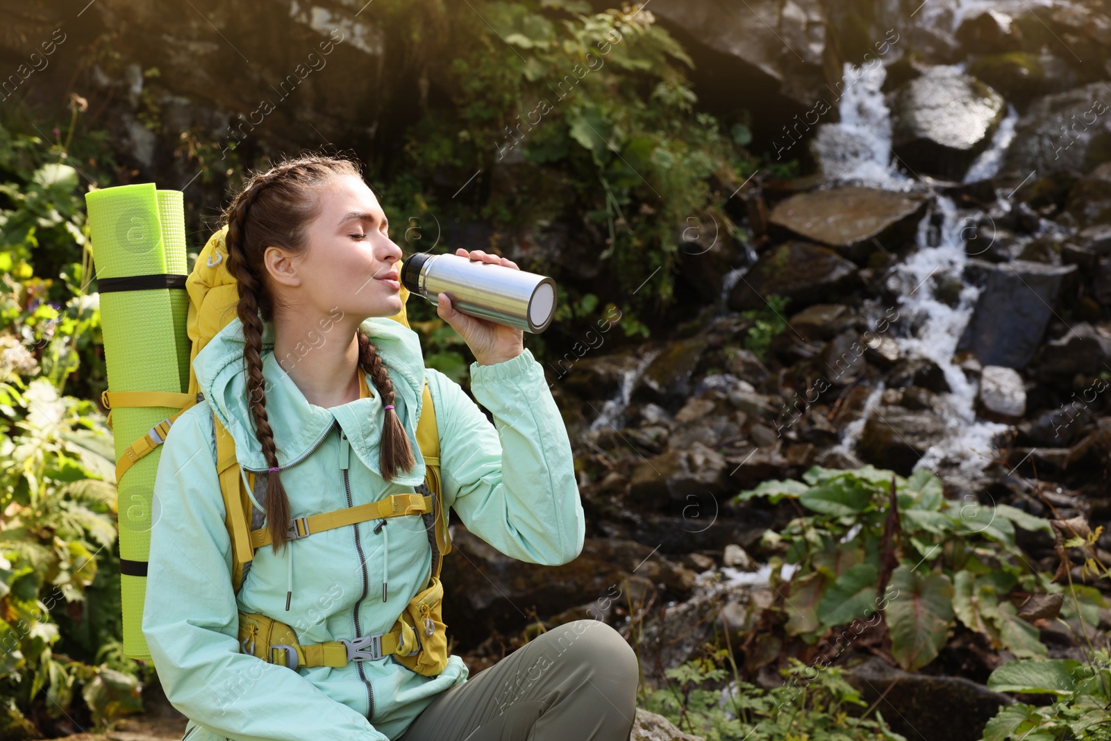 Photo of Tourist with vacuum flask near waterfall in mountains. Space for text