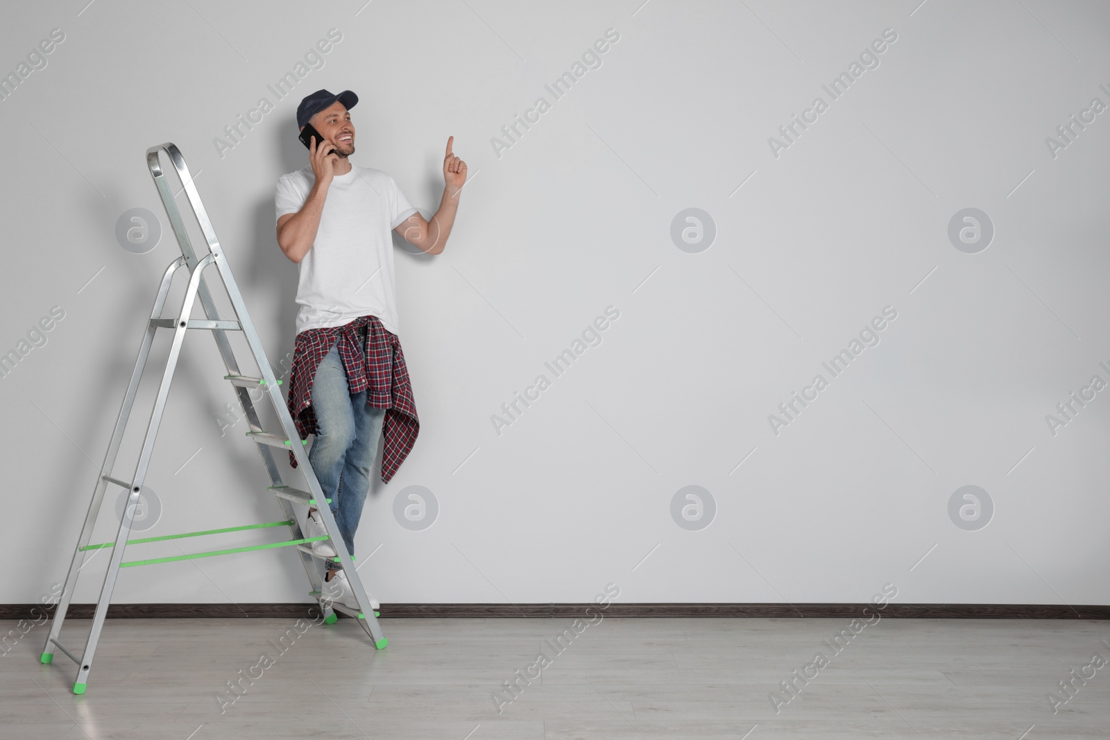 Photo of Handsome man talking on phone near white wall indoors, space for text