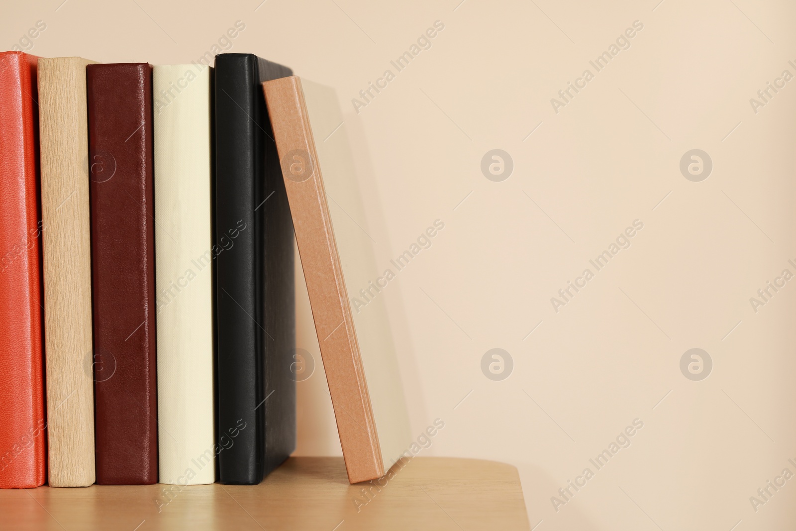 Photo of Different hardcover books on wooden table near beige wall. Space for text