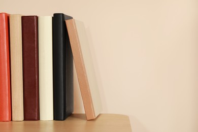 Photo of Different hardcover books on wooden table near beige wall. Space for text