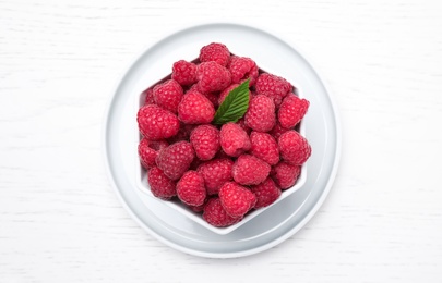 Photo of Delicious fresh ripe raspberries in bowl on white wooden table, top view