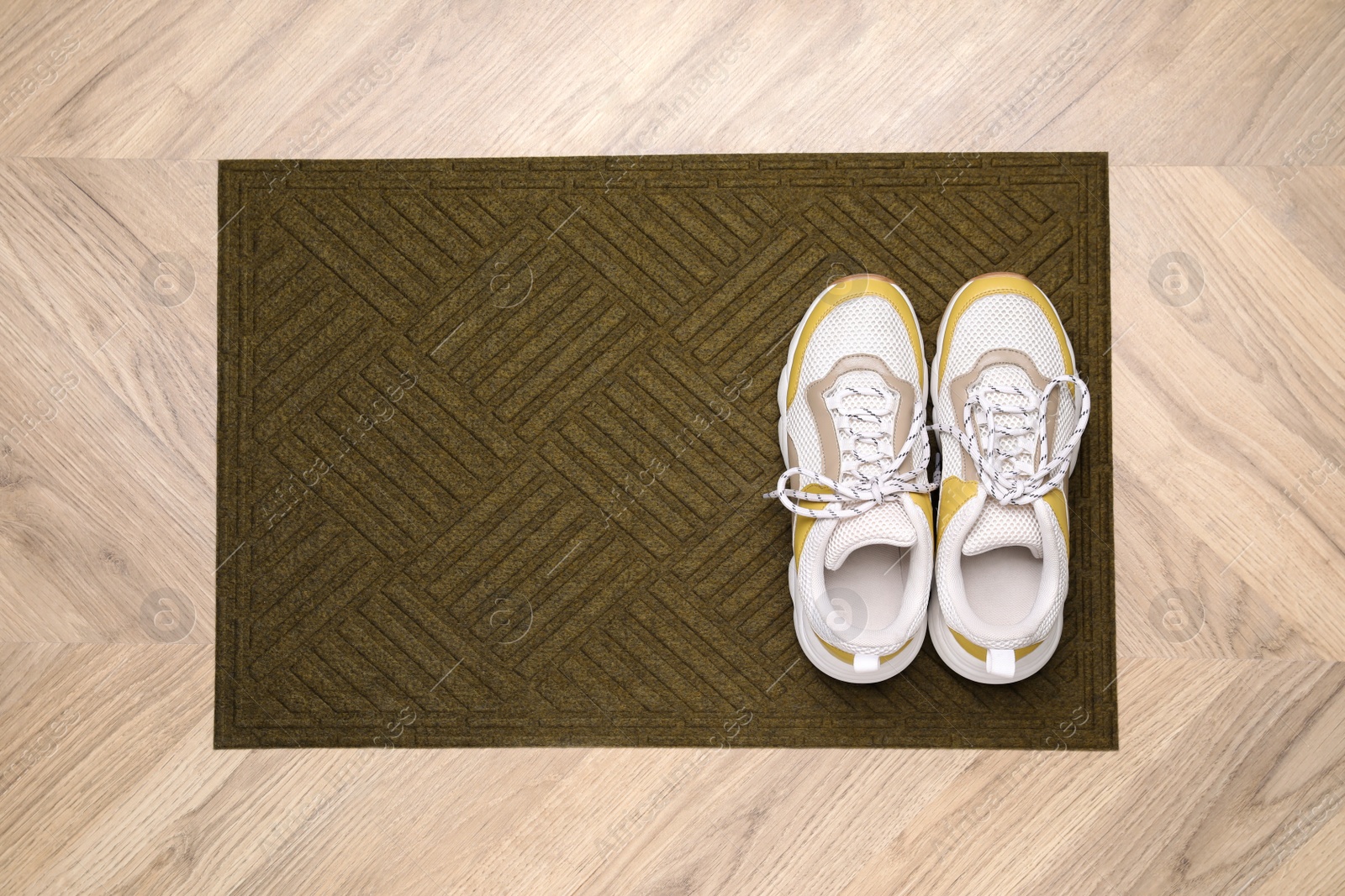 Photo of Stylish door mat and shoes on wooden floor, top view