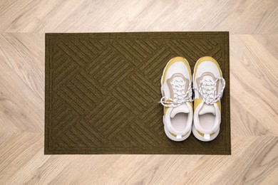 Stylish door mat and shoes on wooden floor, top view