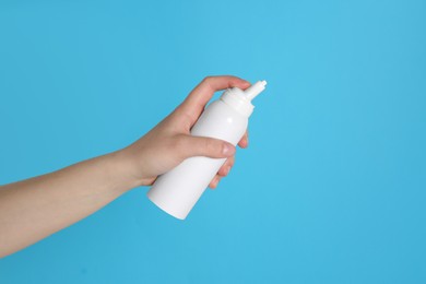 Photo of Woman holding nasal spray on light blue background, closeup