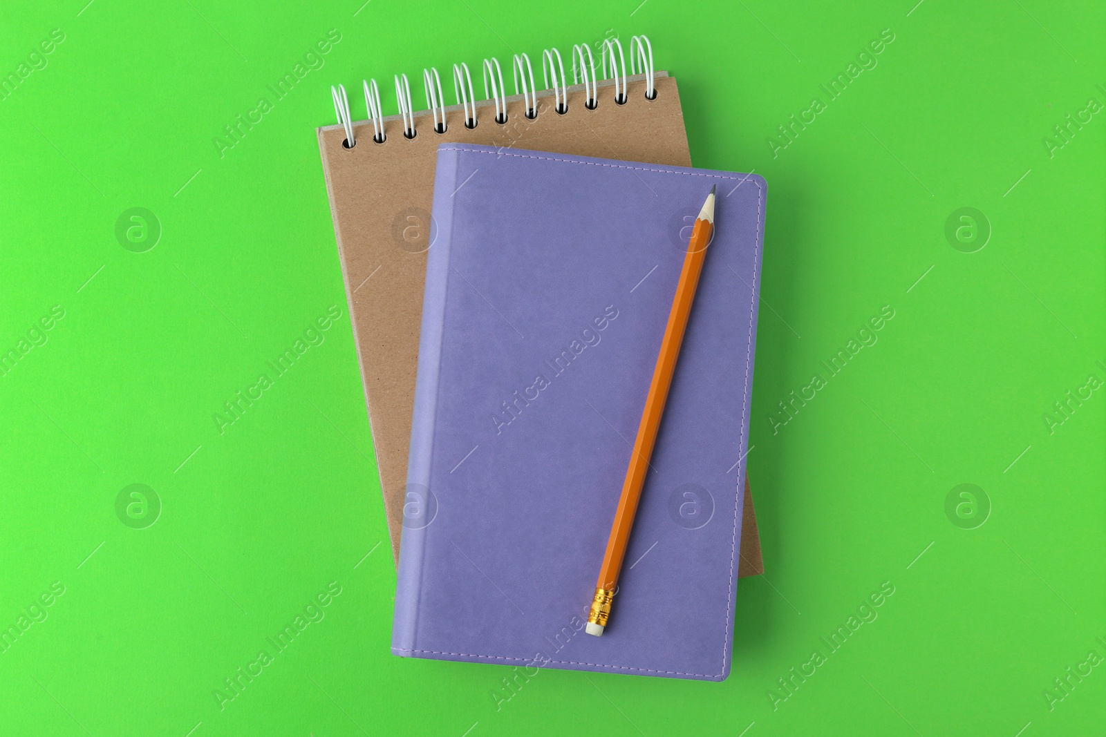 Photo of Notebooks with pencil on light green background, top view