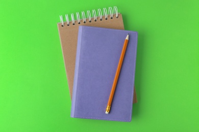 Notebooks with pencil on light green background, top view