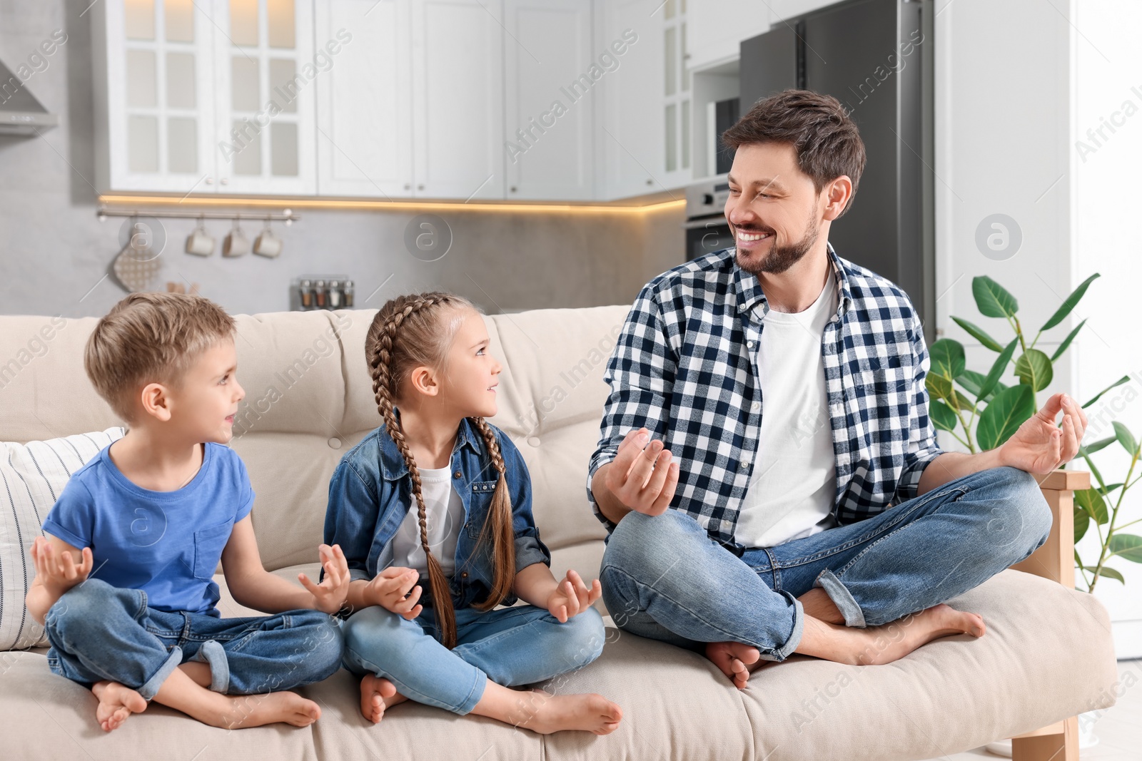 Photo of Father with children meditating together on sofa at home. Harmony and zen