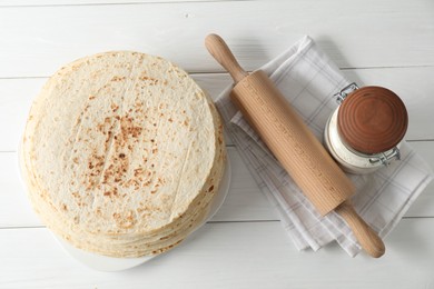 Photo of Tasty homemade tortillas, flour and rolling pin on white wooden table, top view