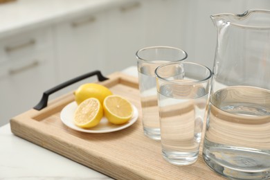 Jug, glasses with clear water and lemons on white table in kitchen, closeup