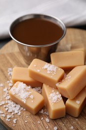 Yummy caramel candies and sea salt on wooden table, closeup