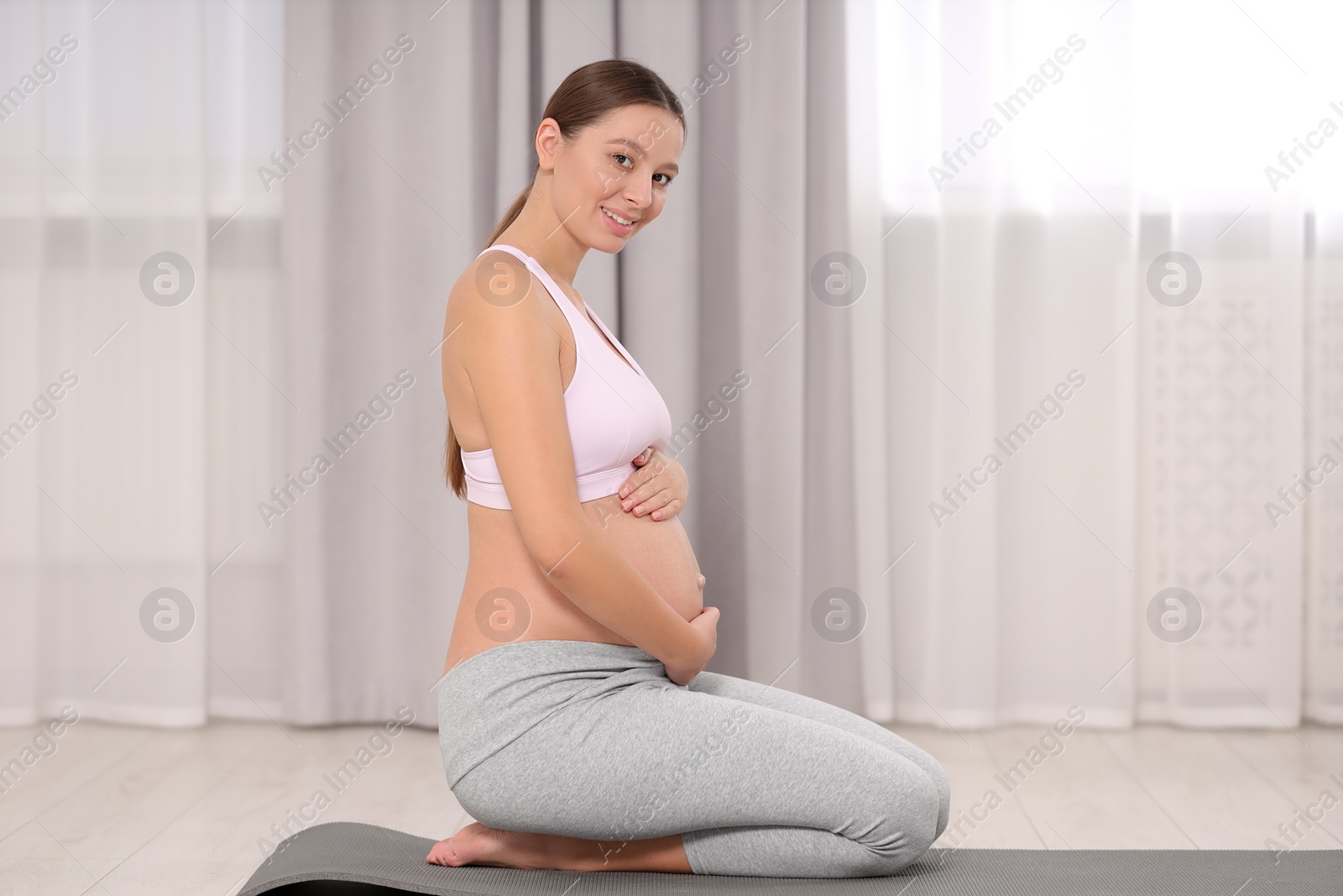 Photo of Pregnant woman sitting on yoga mat at home