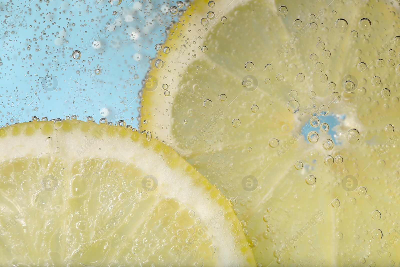 Photo of Juicy lemon slices in soda water against light blue background, closeup