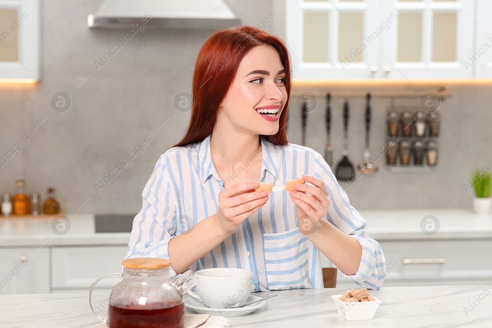 Photo of Happy woman with red dyed hair holding fortune cookie in kitchen