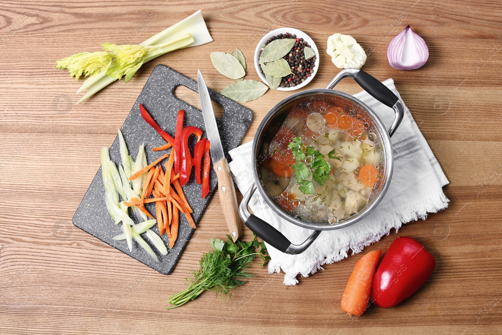 Photo of Pot of delicious vegetable bouillon and ingredients on wooden table, flat lay