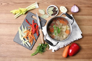 Pot of delicious vegetable bouillon and ingredients on wooden table, flat lay