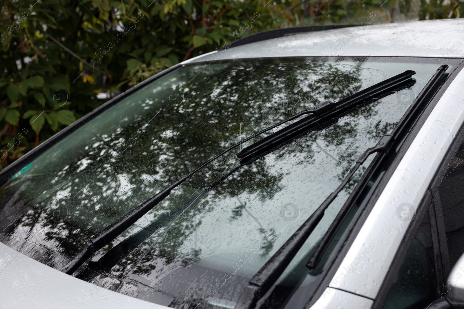 Photo of Wipers cleaning raindrops from car windshield outdoors