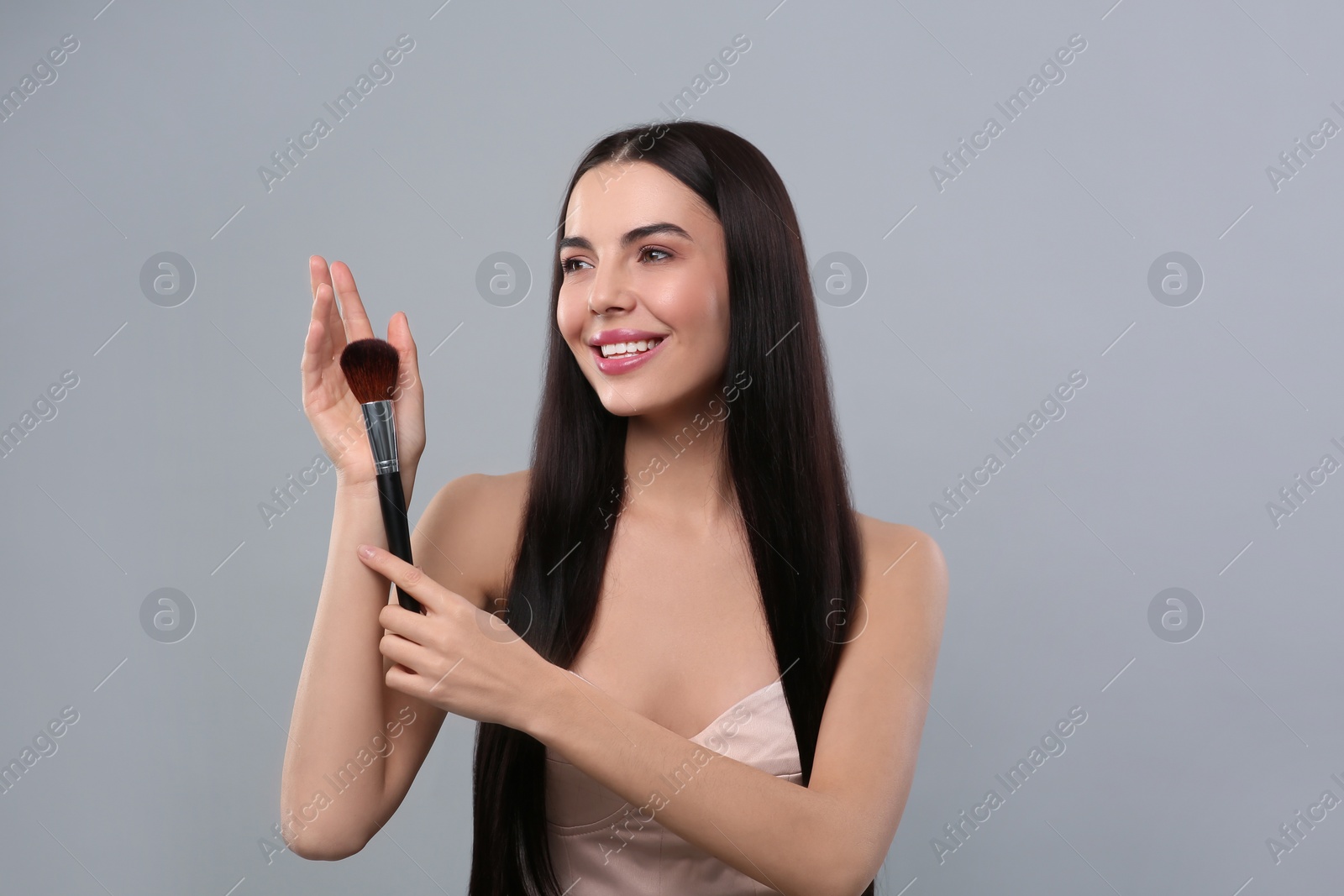 Photo of Happy woman with makeup brush on light grey background