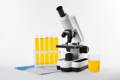Photo of Laboratory ware with urine sample for analysis and microscope on white background