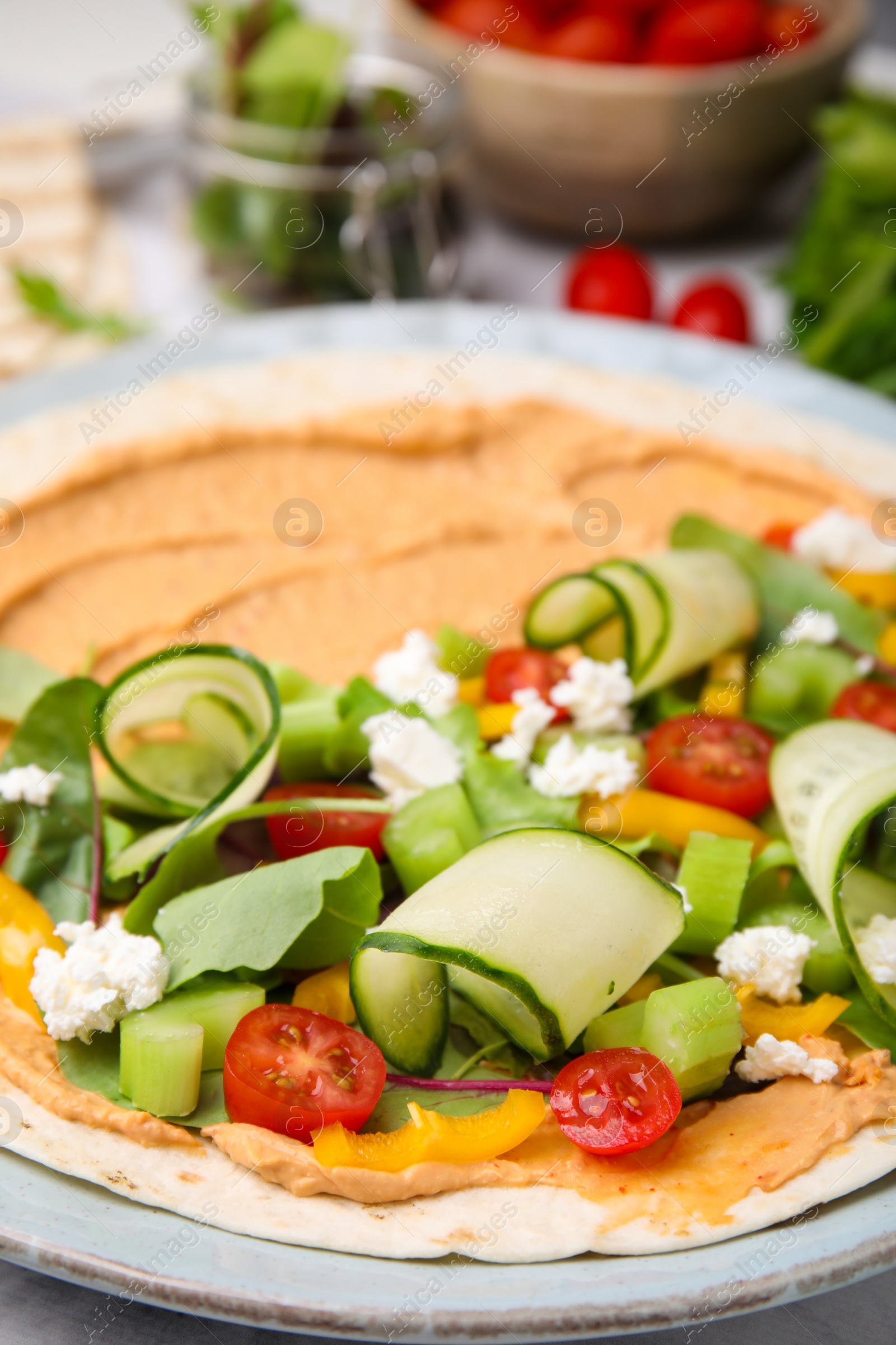 Photo of Tortilla with hummus and vegetables on table, closeup