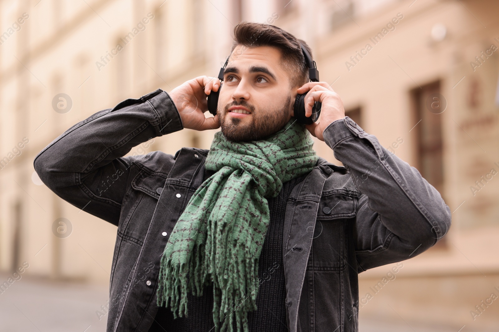 Photo of Smiling man in warm scarf listening to music outdoors