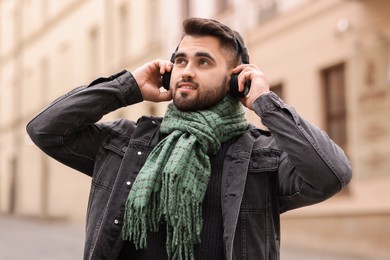 Photo of Smiling man in warm scarf listening to music outdoors