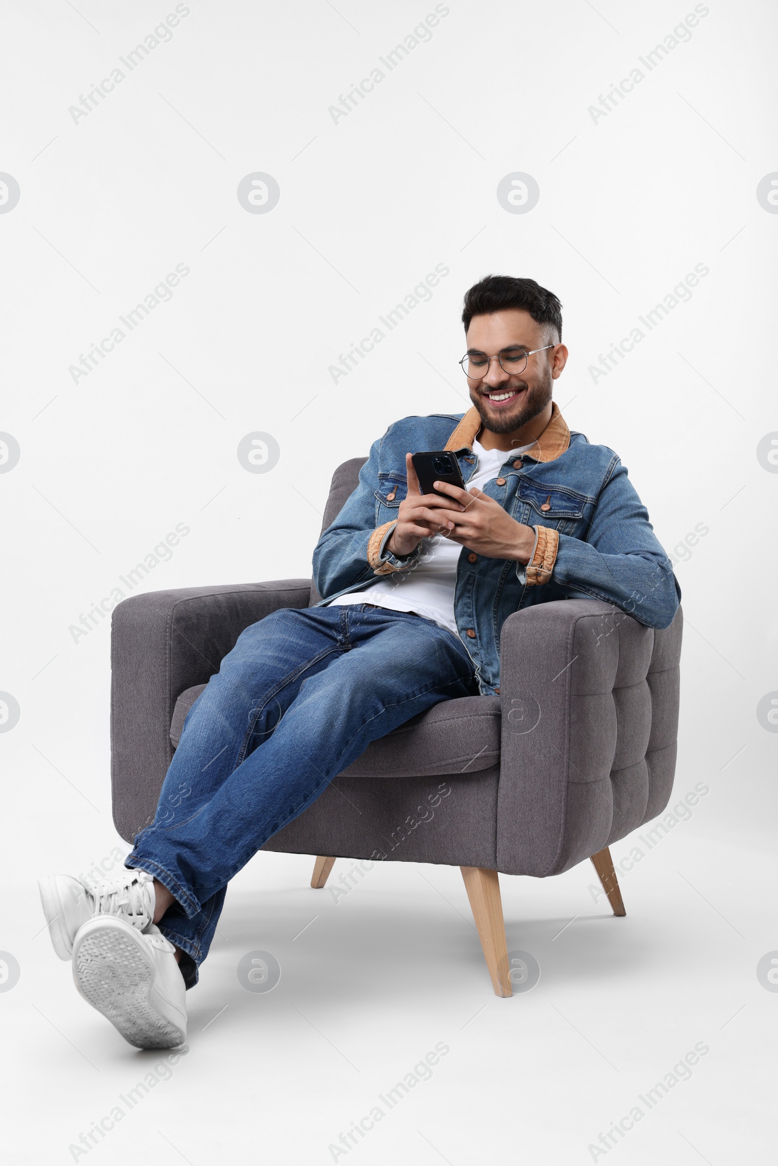 Photo of Happy man using smartphone in armchair on white background