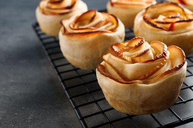 Photo of Cooling rack with freshly baked apple roses on grey table, closeup. Beautiful dessert