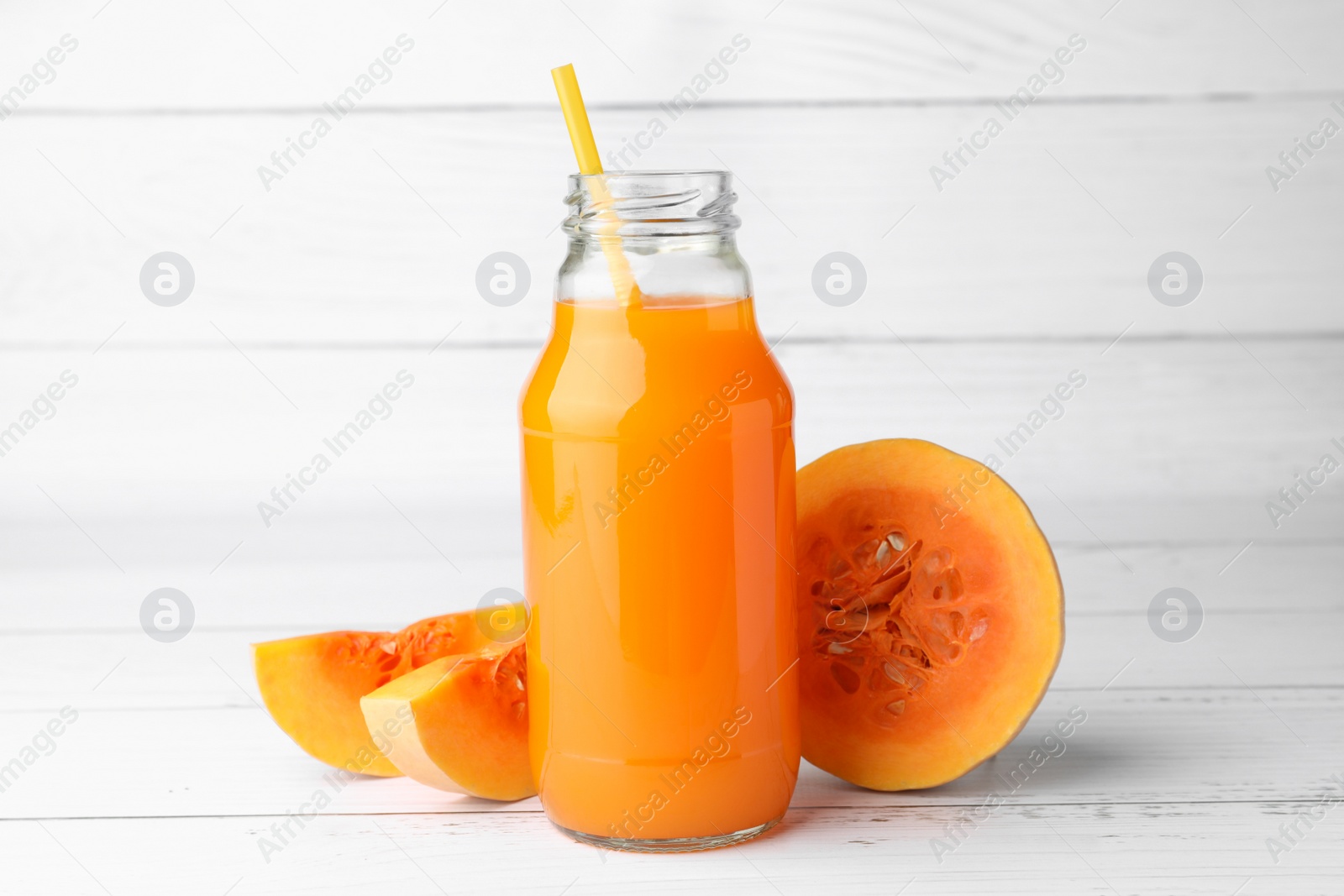 Photo of Tasty pumpkin juice in glass bottle and cut pumpkin on white wooden table