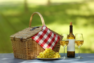 Wicker basket with blanket, wine and grapes on table in park. Summer picnic