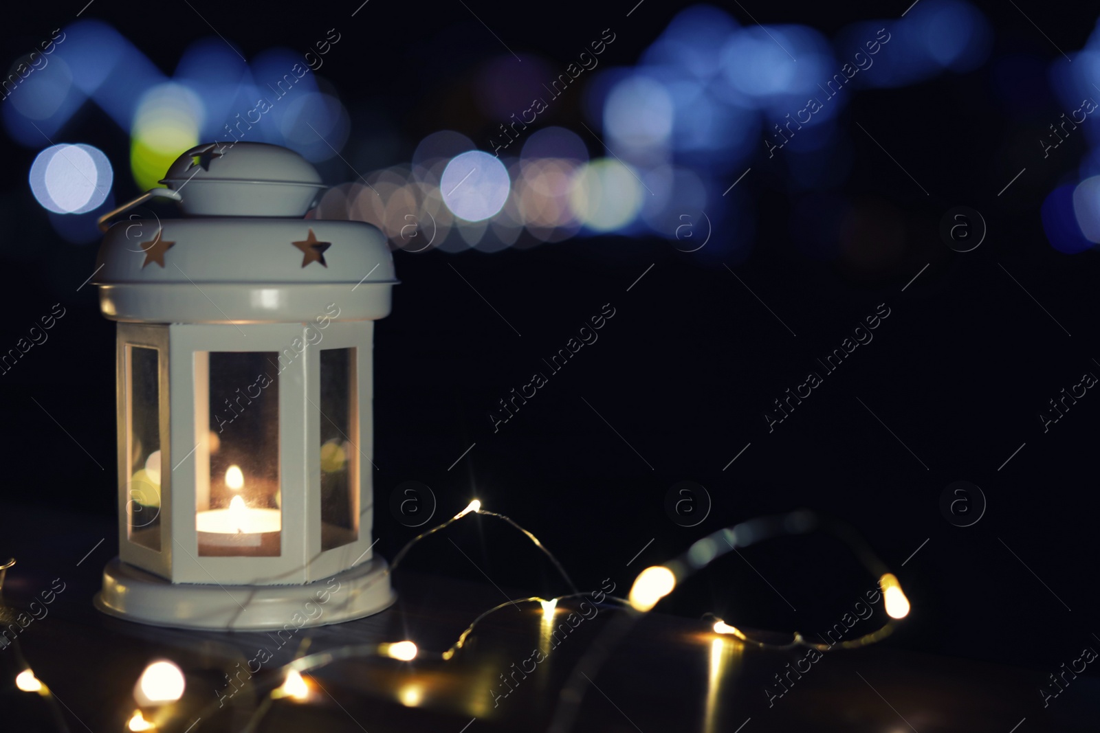 Photo of Lantern and Christmas lights on wooden railing outdoors against blurred background, space for text. Winter night