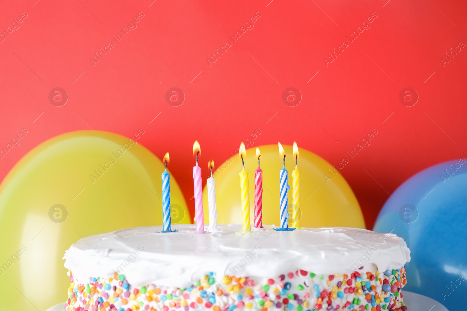 Photo of Tasty birthday cake with burning candles and balloons on red background, space for text