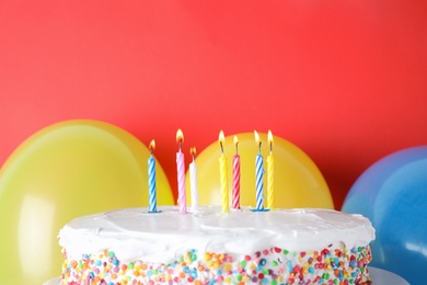 Tasty birthday cake with burning candles and balloons on red background, space for text